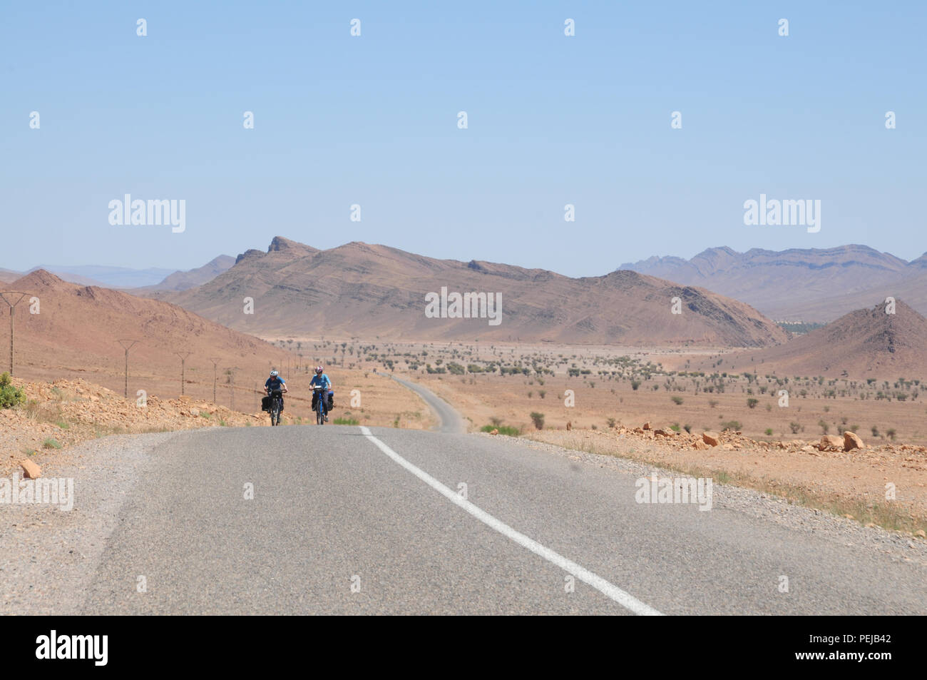 Two cyclists make their way along a road on the edge of the Sahara in Morocco, heading between Tata and Igherm on the edge of the anti Atlas mountains. Stock Photo