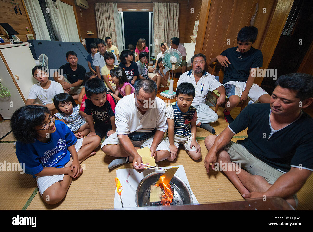 Sousei Yamakawa, owner of the house, burns uchikabi, money of the other world, while surrounded by relatives in Yomitan village, Okinawa, Japan, Aug. 28, 2015. Okinawans invite their ancestral spirits to visit the family's Buddhist altar during this traditional period. (U.S. Air Force photo by Naoto Anazawa) Stock Photo