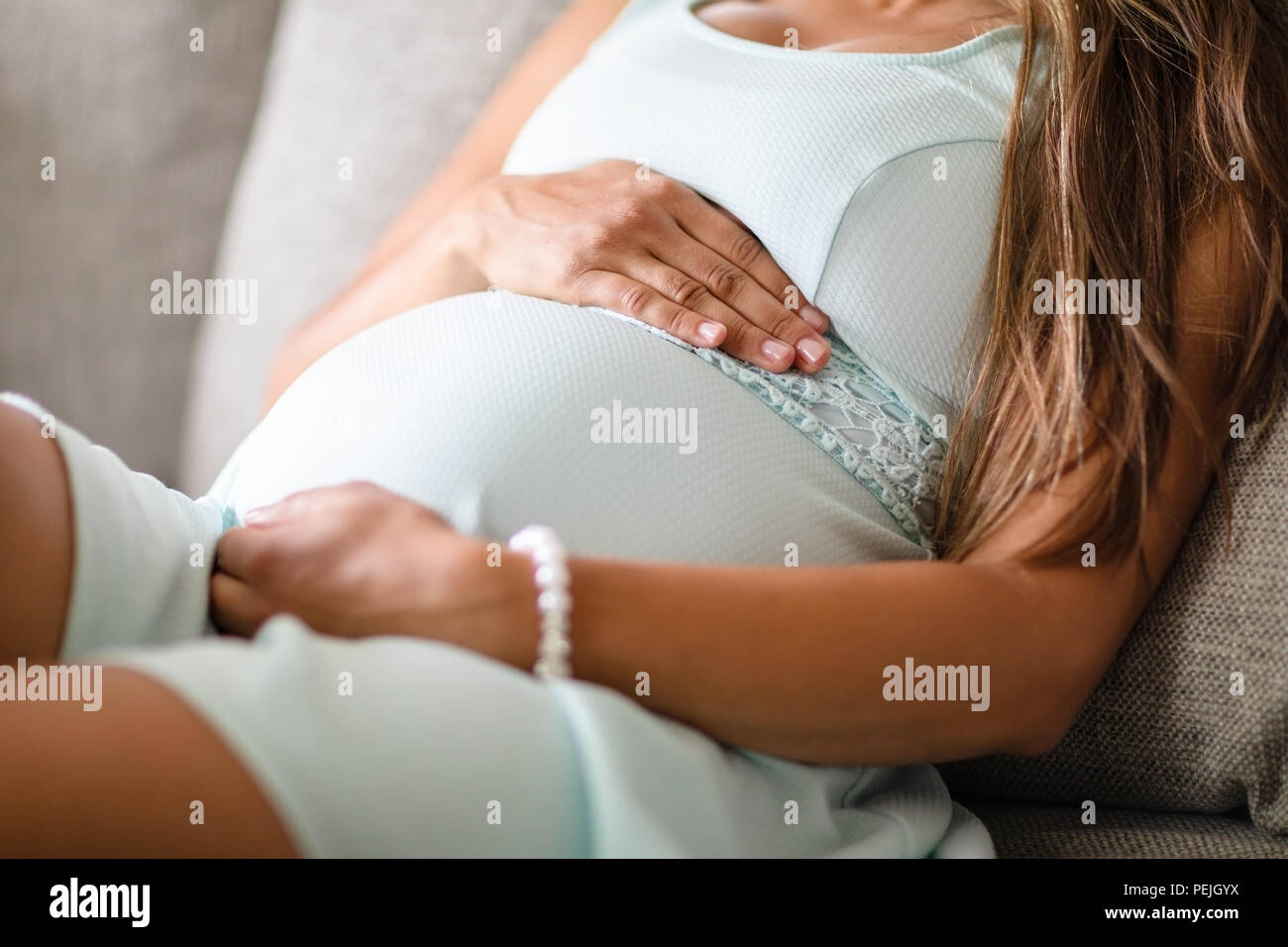 Closeup of pregnant woman sitting in sofa with her hands at belly
