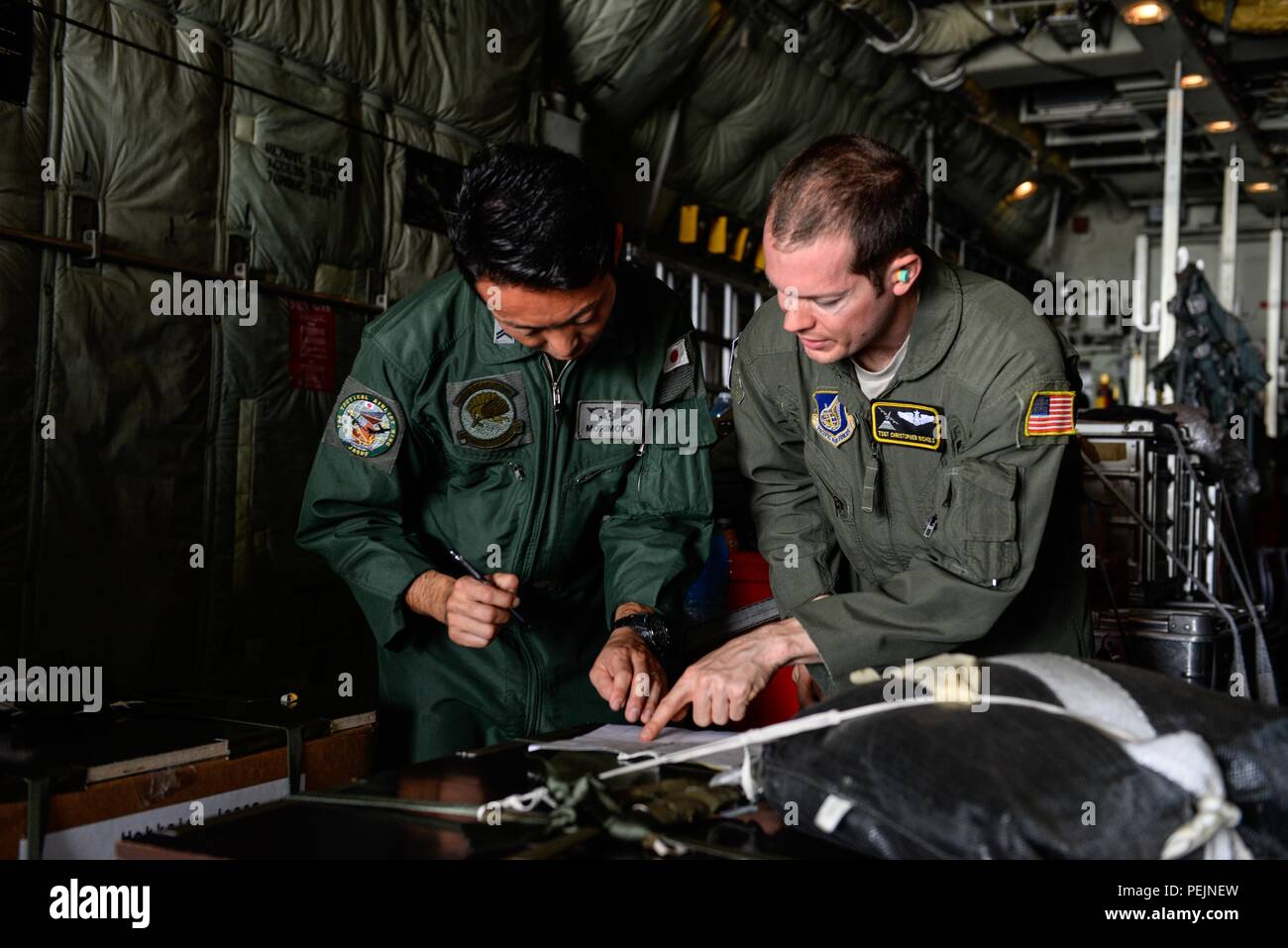 Japan Air Self-Defense Force Tech. Sgt. Satoshi Marimoto, left, and U.S. Air Force Tech. Sgt. Christopher Nichols, both C-130 loadmasters, review load documents before Operation Christmas Drop flight SANTA12 Dec. 8, 2015, at Andersen Air Force Base, Guam. The 2015 Christmas Drop missions mark the first time the event includes trilateral air support from the JASDF and Royal Australian Air Force. Operation Christmas Drop is a humanitarian aid/disaster relief training event where C-130 aircrews perform low-cost, low-altitude airdrops on unsurveyed drop zones while providing critical supplies to 5 Stock Photo