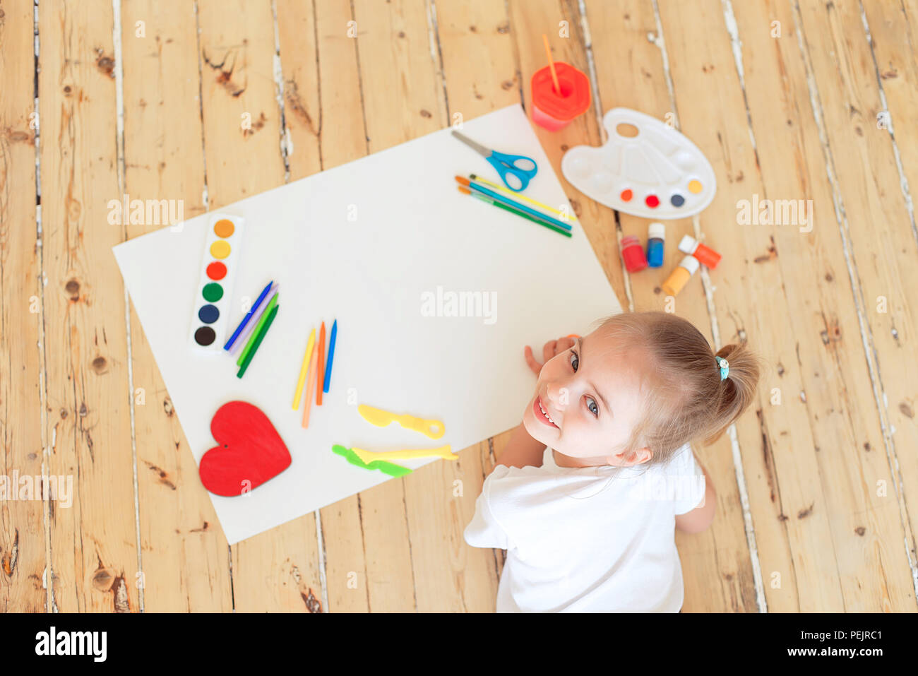 Top view of little blonde girl painting on big white paper while laying ...