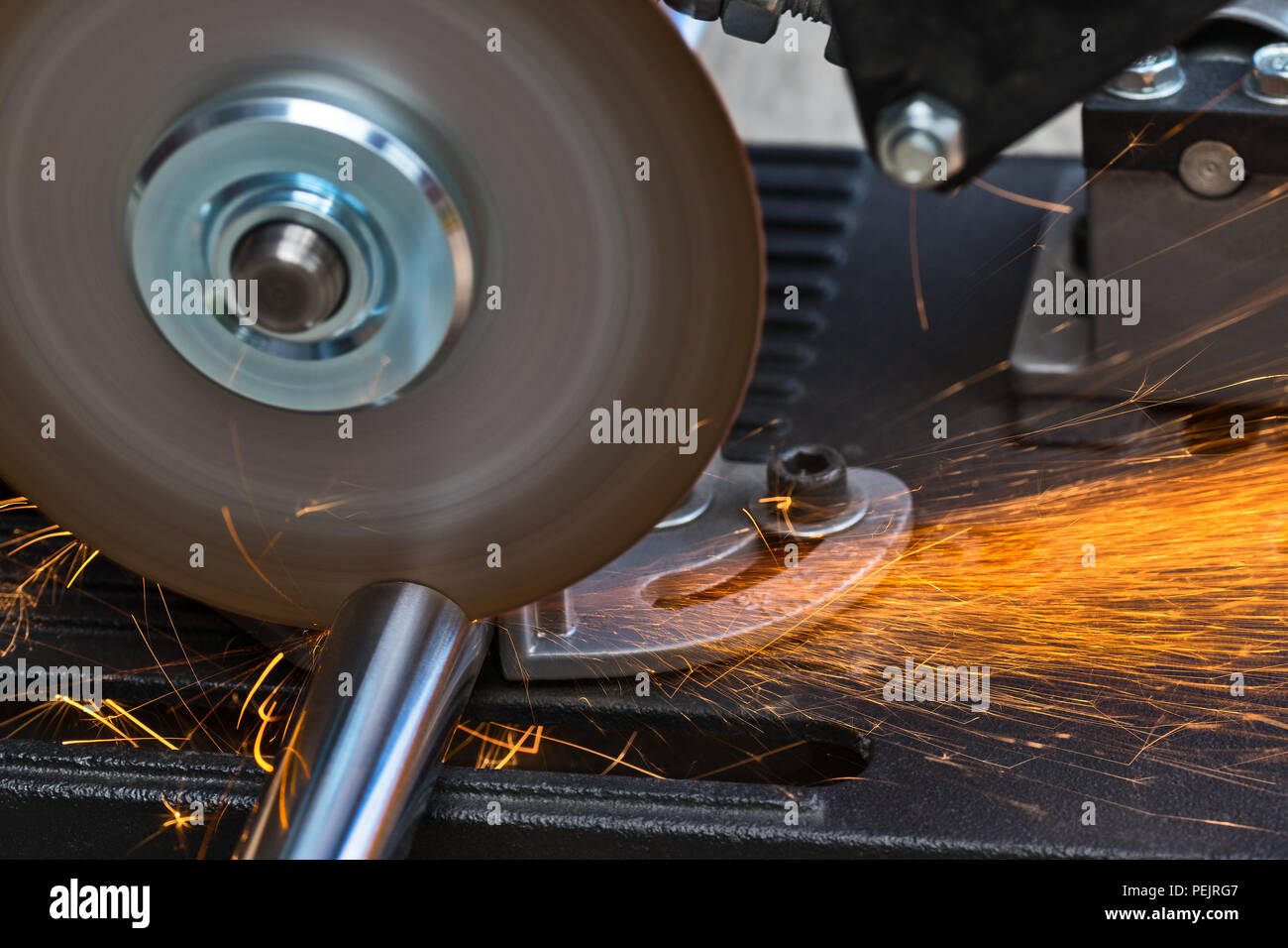 Cutting a metallic rod by a circular saw machine. Close-up of hot flying sparks when sawing a steel workpiece. Motion blur of disc with sharp blade. Stock Photo