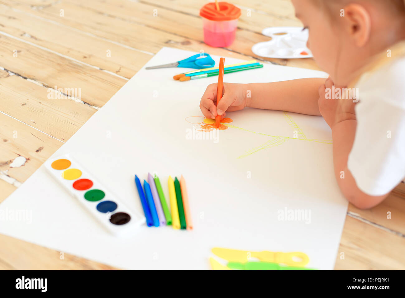 Little blonde girl painting on big white paper while laying on the ...