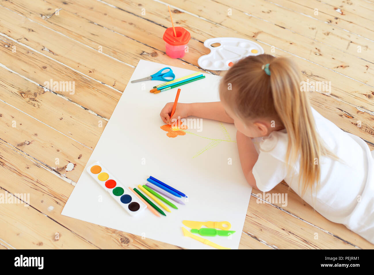 Top view of little blonde girl painting on big white paper while laying ...