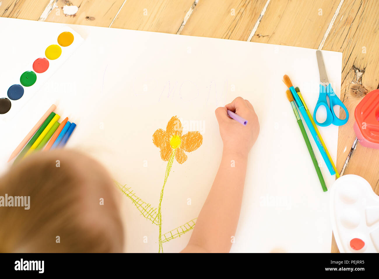 Little blonde girl painting on big white paper while laying on the ...