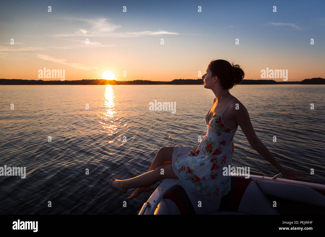 Young woman sitting on the edge of a boat on a lake at sunset Stock ...