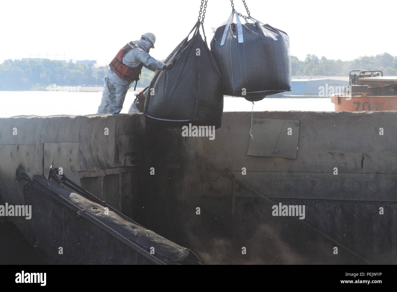 Super sacks of powdered and granular activated carbon are added to a scow of dredged sediment before mixing with a clamshell bucket. Stock Photo