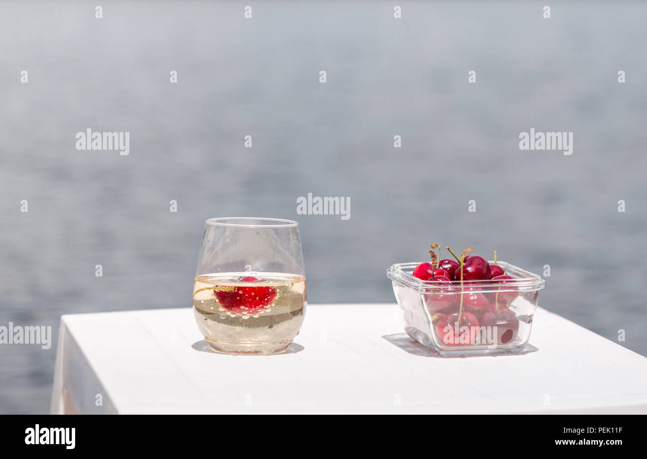 A bowl of cherries and a glass of champagne next to the lake. Stock Photo