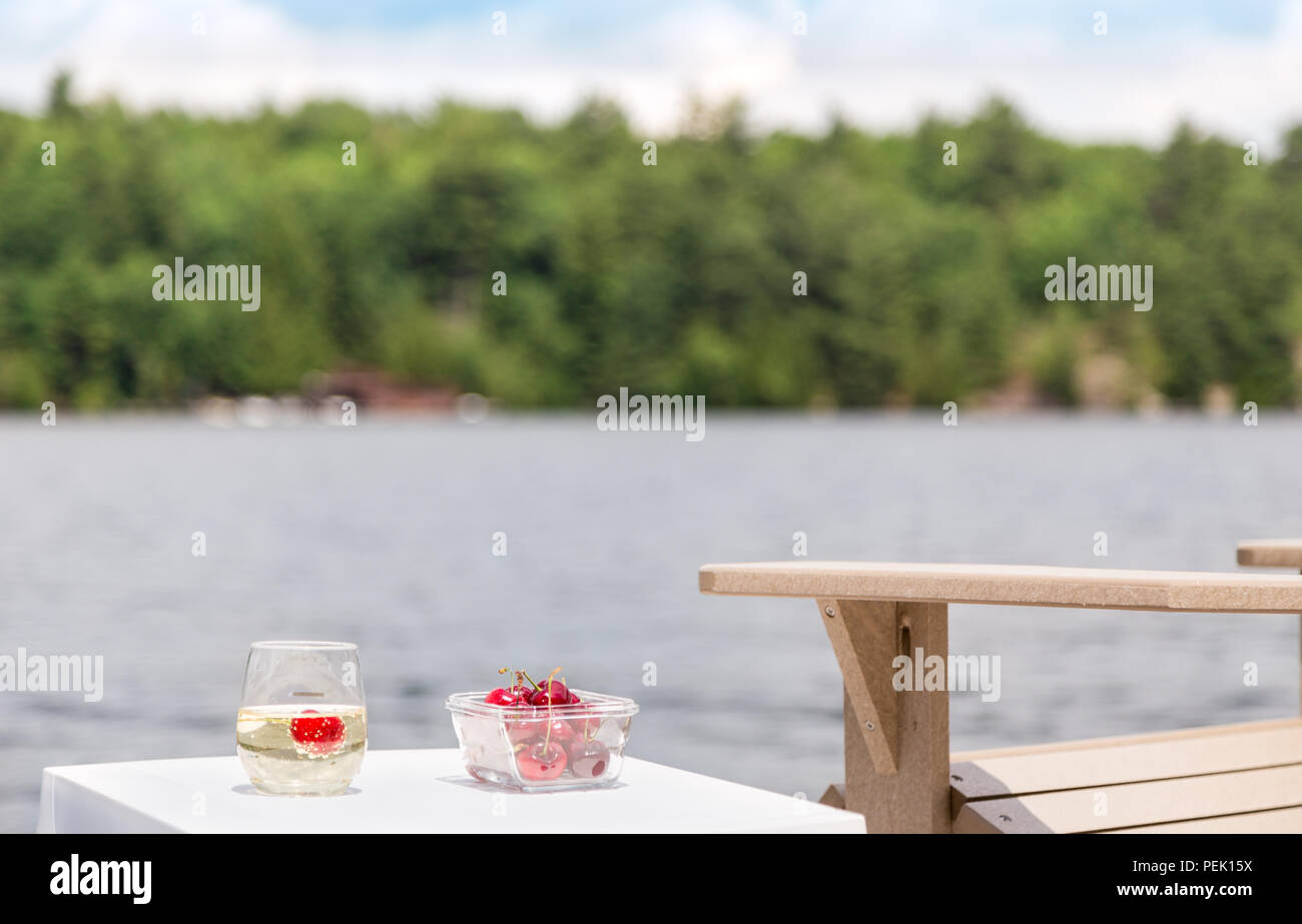 A bowl of cherries and a glass of champagne next to the lake. Stock Photo