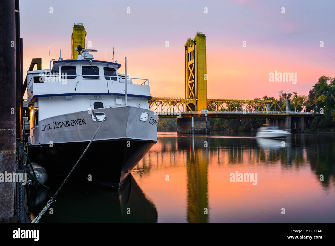 The Capitol Hornblower docked in Old Sacramento as the sun rises over the Tower Bridge and the Sacramento River in Sacramento, California. Stock Photo
