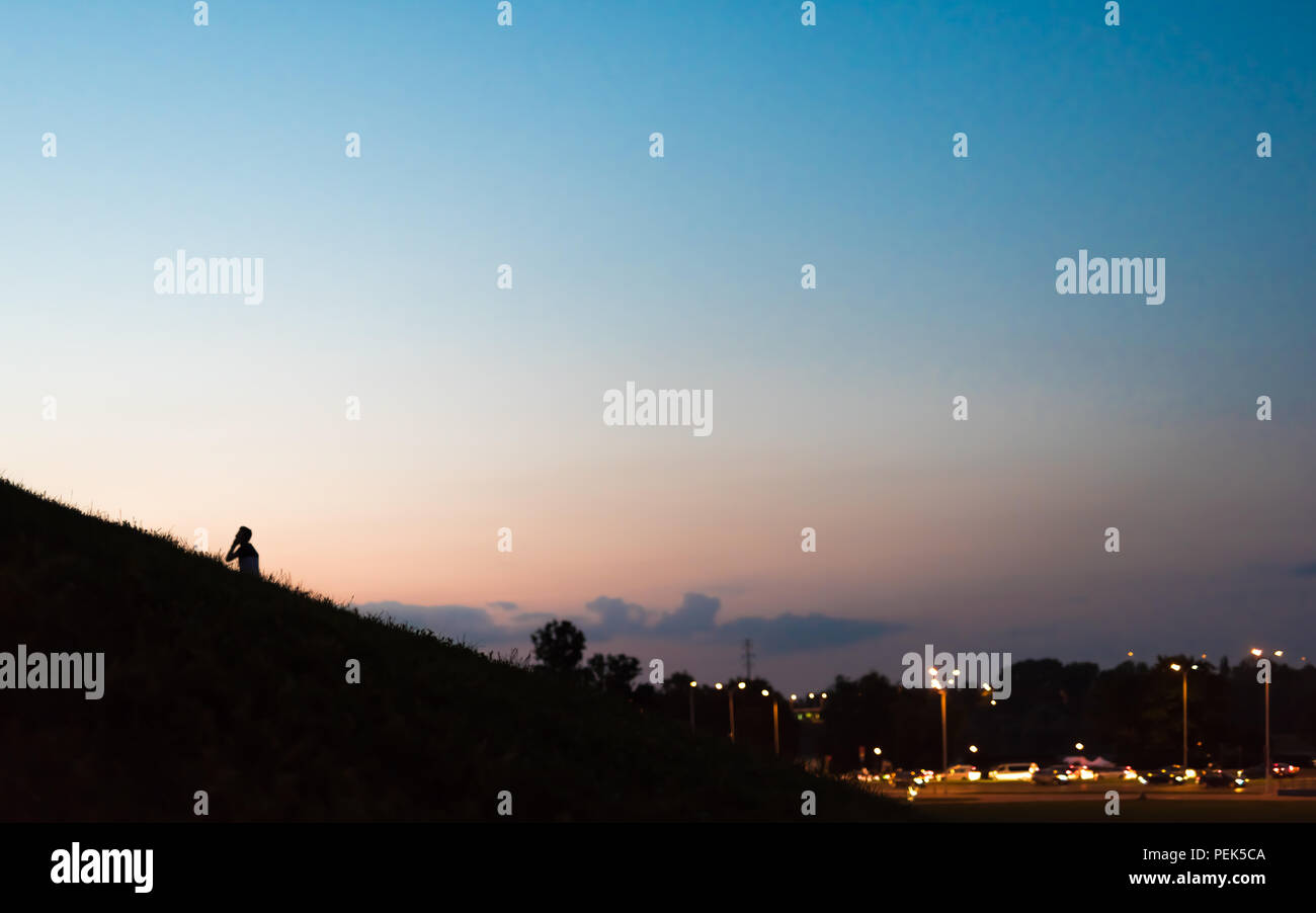 A boy with a mobile phone walks up a hill in the evening Stock Photo