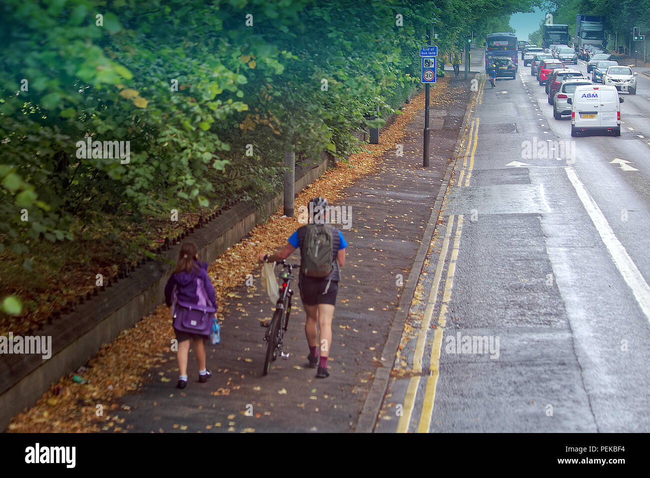 father and daughter walking to school on first day of term on pavement sidewalk pushing bike next to road traffic Stock Photo