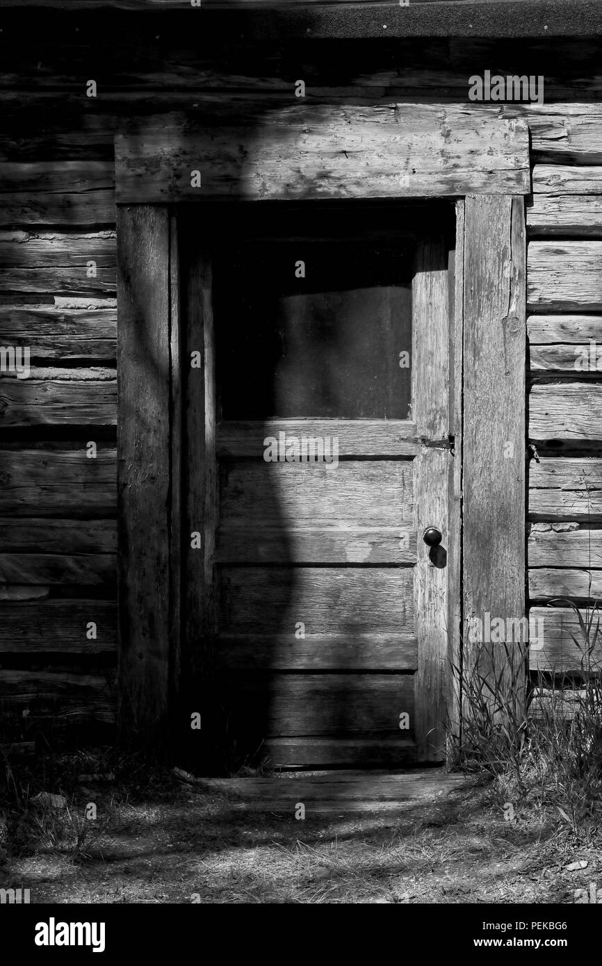 Cabin Door and Siding: Black and white photo, sunlight and shadows tease the weathered door in this early morning photo taken in a Montana ghost town. Stock Photo