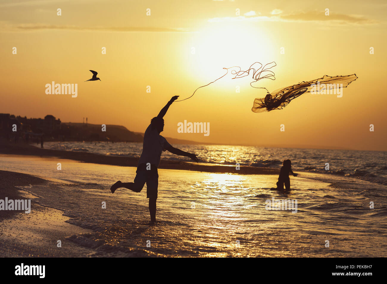 Silhouette of a fisherman at sunset throwing a fishing net into the sea  Stock Photo - Alamy