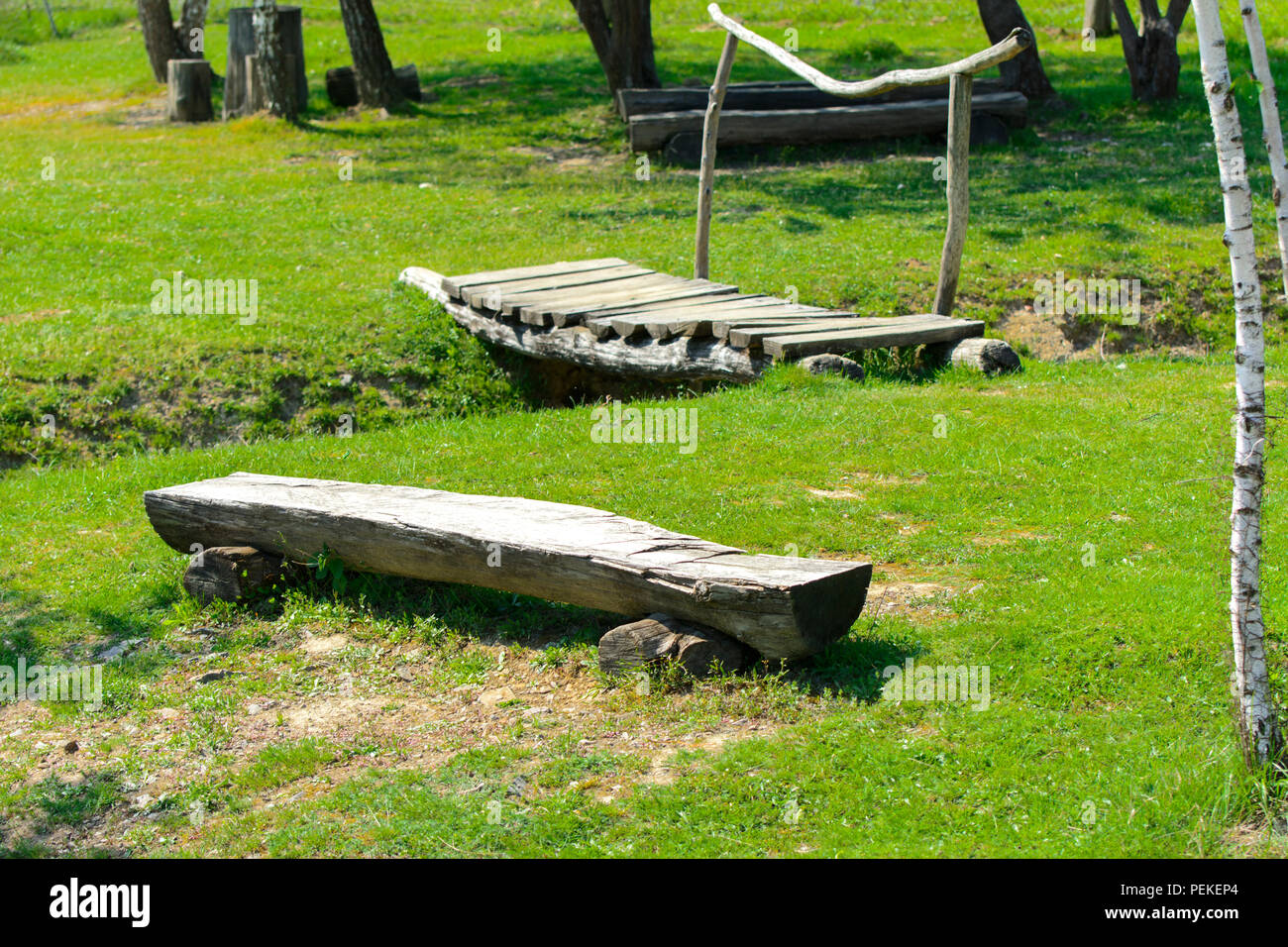 An old wooden bench rudely made from a log of wood against a background of green grass. Stock Photo