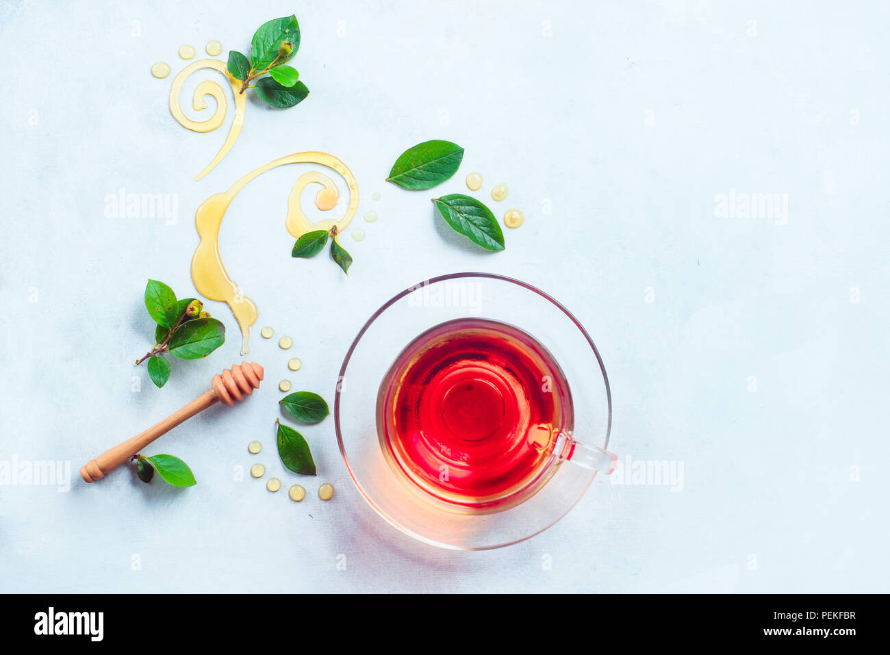 Glass cup of tea with decorative honey swirls and green leaves. Home remedies flat lay on a white background with copy space Stock Photo