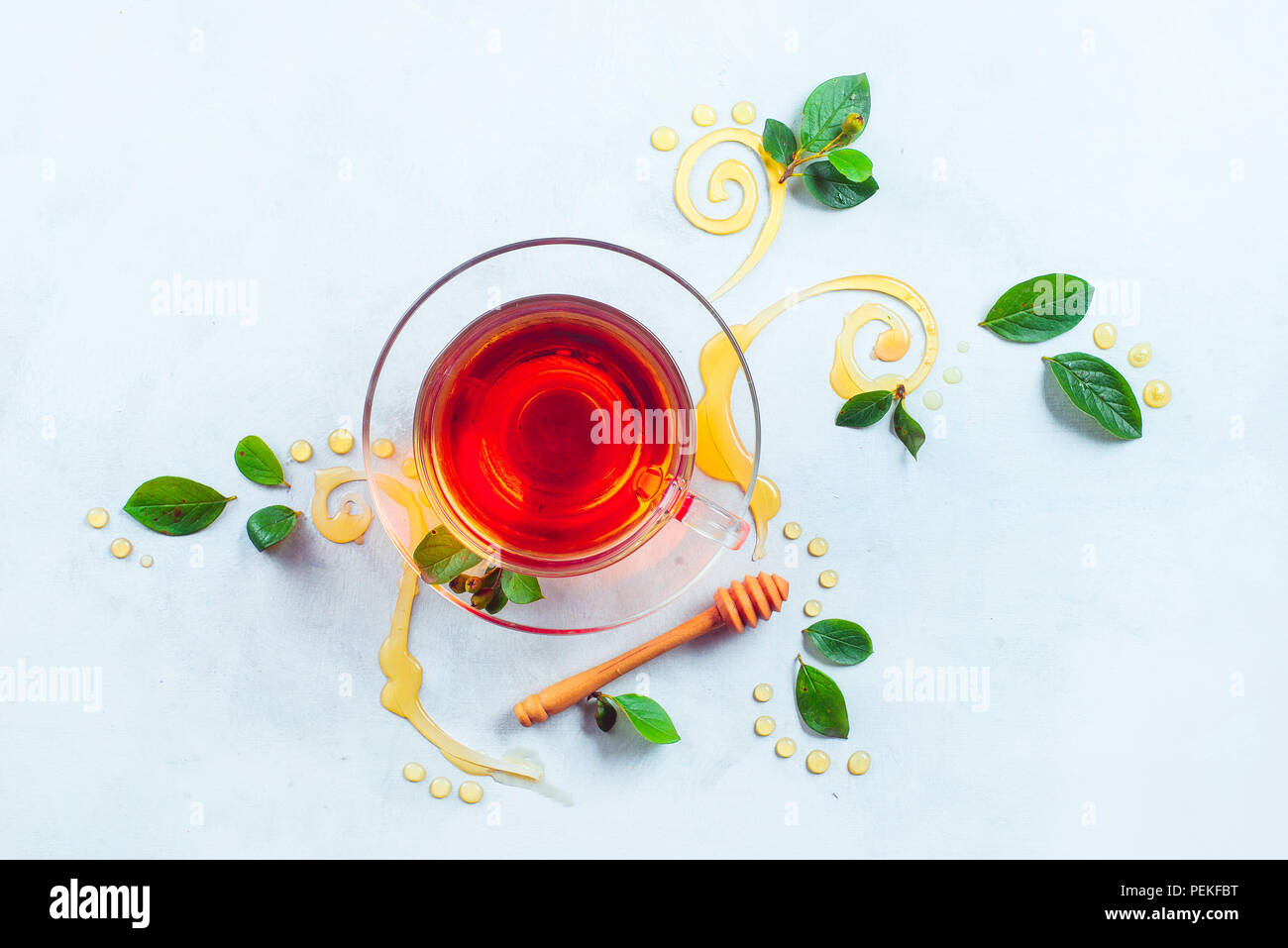 Glass cup of tea with decorative honey swirls and green leaves. Home remedies flat lay on a white background with copy space Stock Photo
