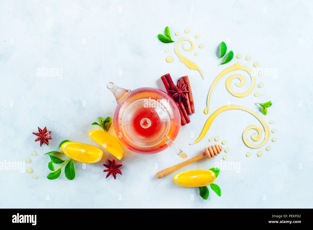 Honey and tea header. Glass teapot with decorative honey swirls, lemon slices and green leaves. Home remedies flat lay on a white background with copy Stock Photo