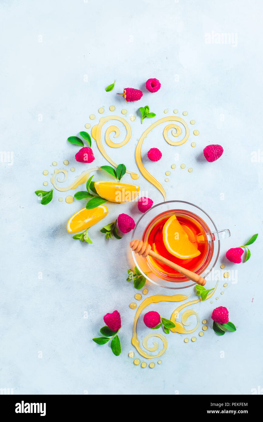Honey tea from above. Decorative honey swirls, lemon slices, berries and tea in a glass cup on a white wooden background with copy space. Creative foo Stock Photo