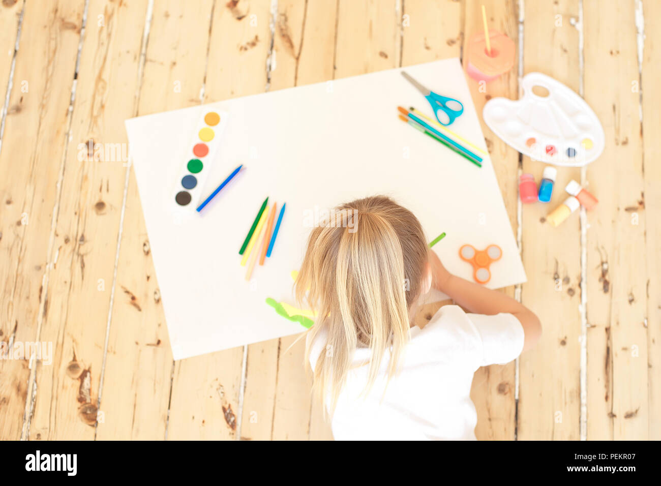 Top view of little blonde girl painting on big white paper while laying ...