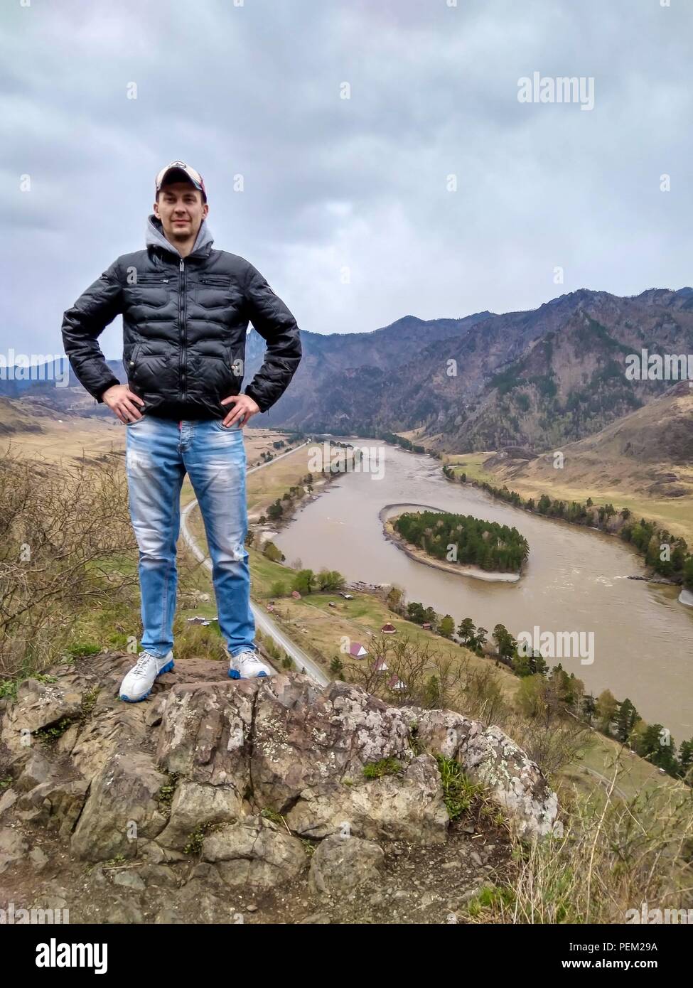 Young man in the cap is standing on the edge of a cliff in Altai ...