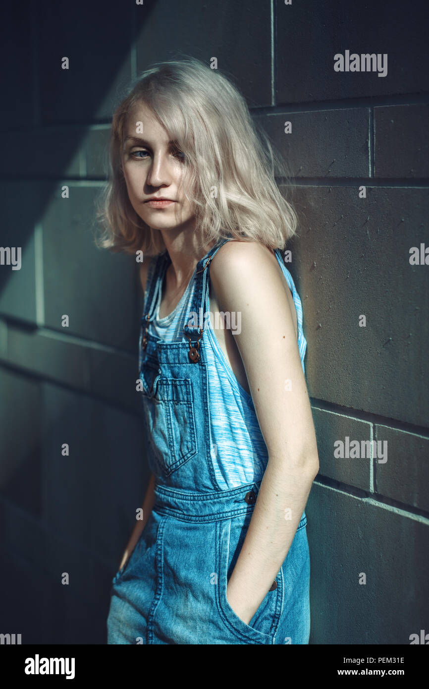 Portrait of beautiful Caucasian teenage young blonde alternative slim anorexic model girl woman in blue tshirt, jeans romper with her hands in pockets Stock Photo