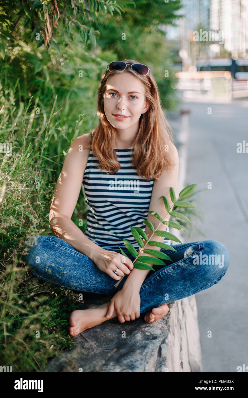 beautiful smiling white Caucasian girl woman with long blonde hair and blue  eyes wearing striped t- shirt and jeans outside in summer park among green  Stock Photo - Alamy