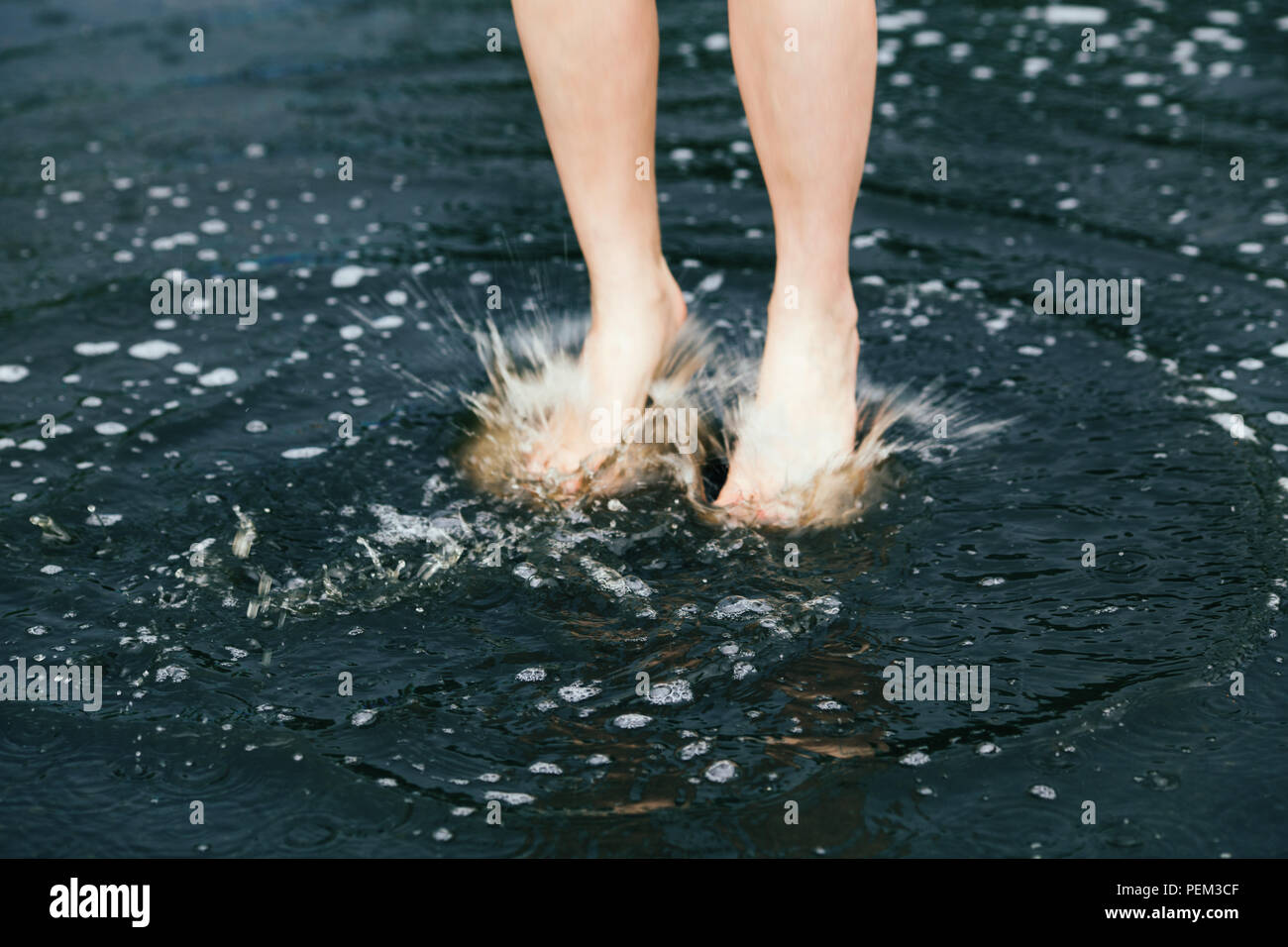 Closeup of legs feet of young girl woman jumping in puddles water