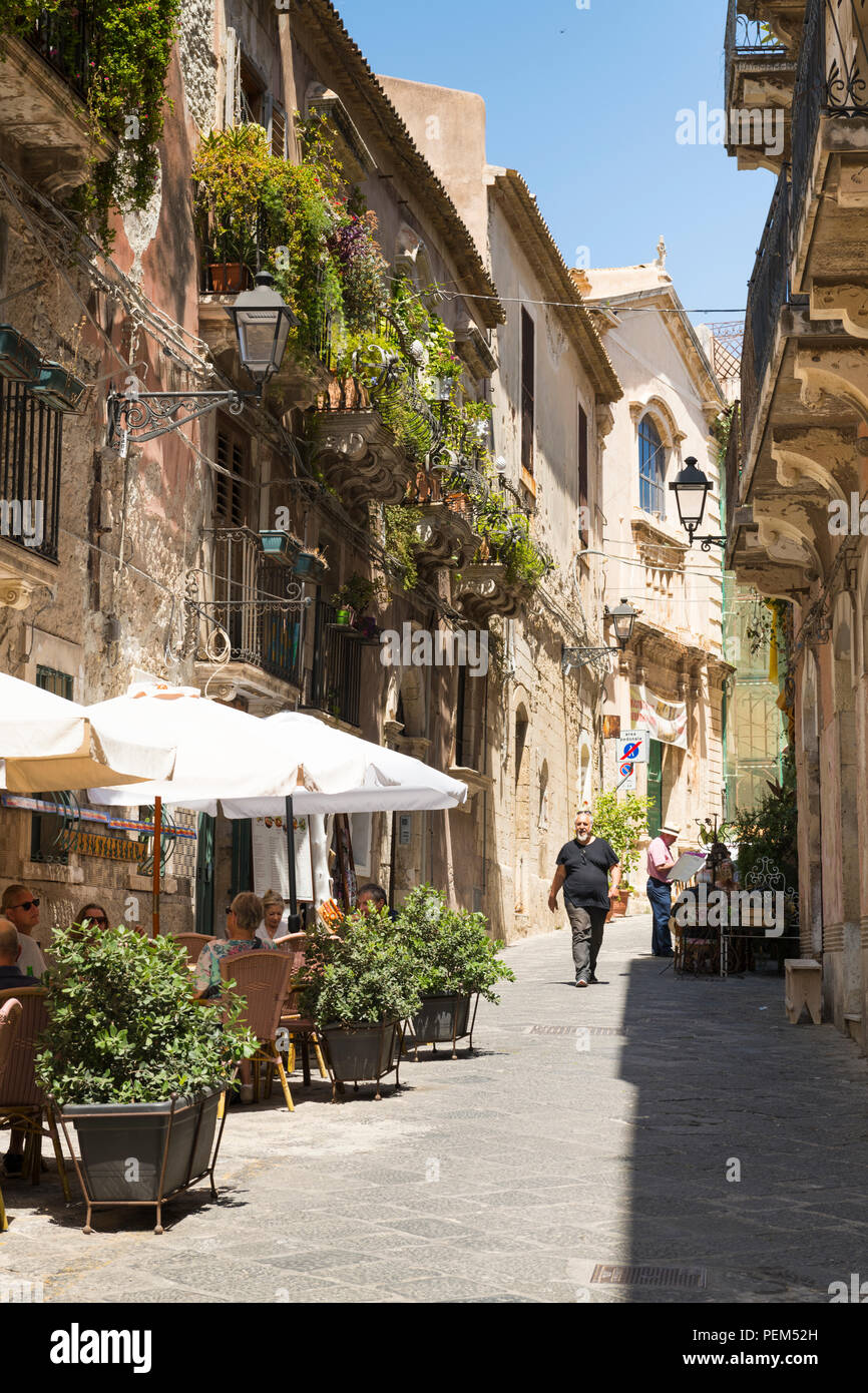 Italy Sicily Syracuse Siracusa Ortygia typical old town narrow street restaurant trattoria diners parasols planters balconies street lights Stock Photo