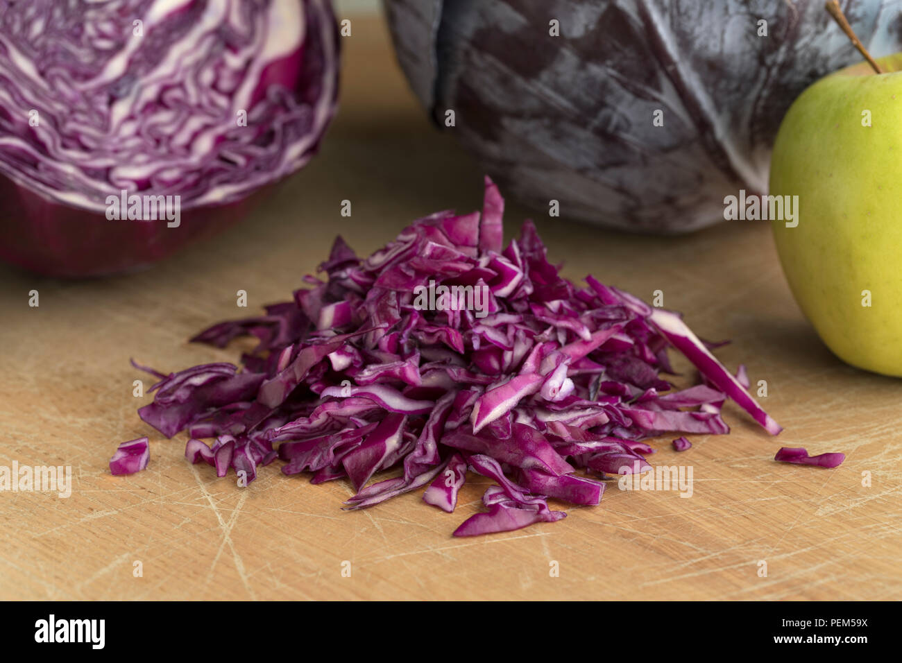 Heap of fresh raw shredded red cabbage with a whole one and apple in the background Stock Photo