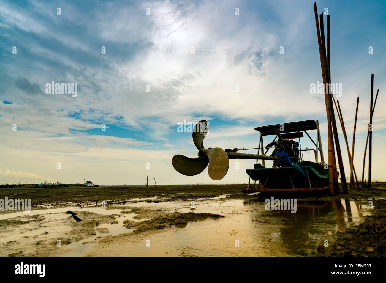 Blade boat on sea coast with blue sky and white clouds at boatyard. Propeller of longtail boat at dock hull. Dry bamboo pole embroidered on the mud be Stock Photo