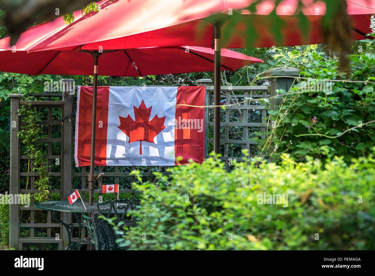 A Canada flag hangs on a fence under two red umbrellas. Stock Photo