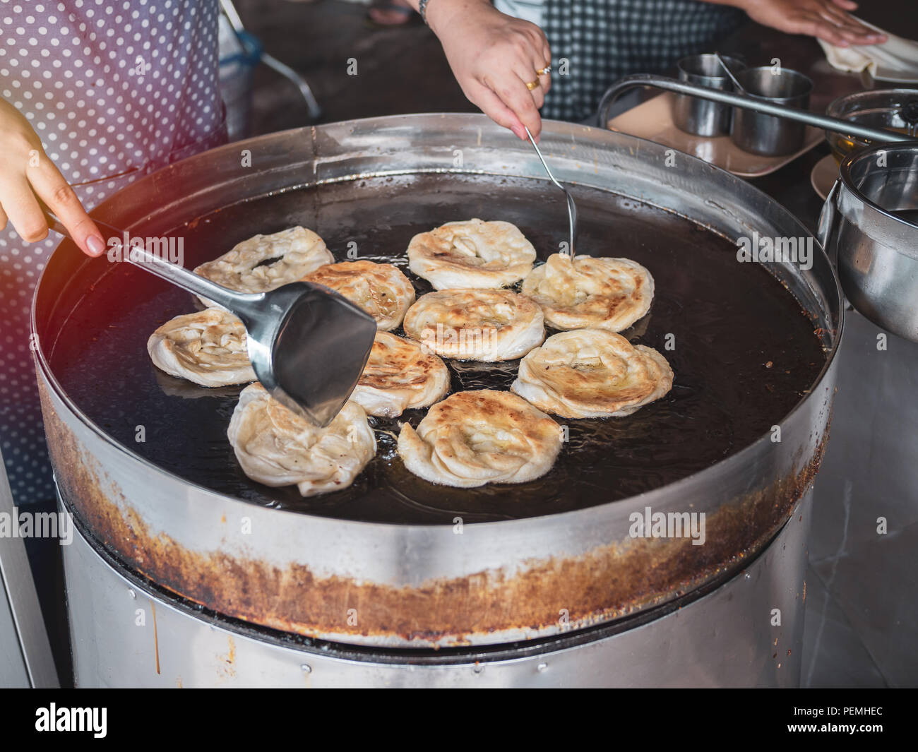 Fried indian bread roti in big pan. Hands making traditional indian food. Roti oil. Stock Photo