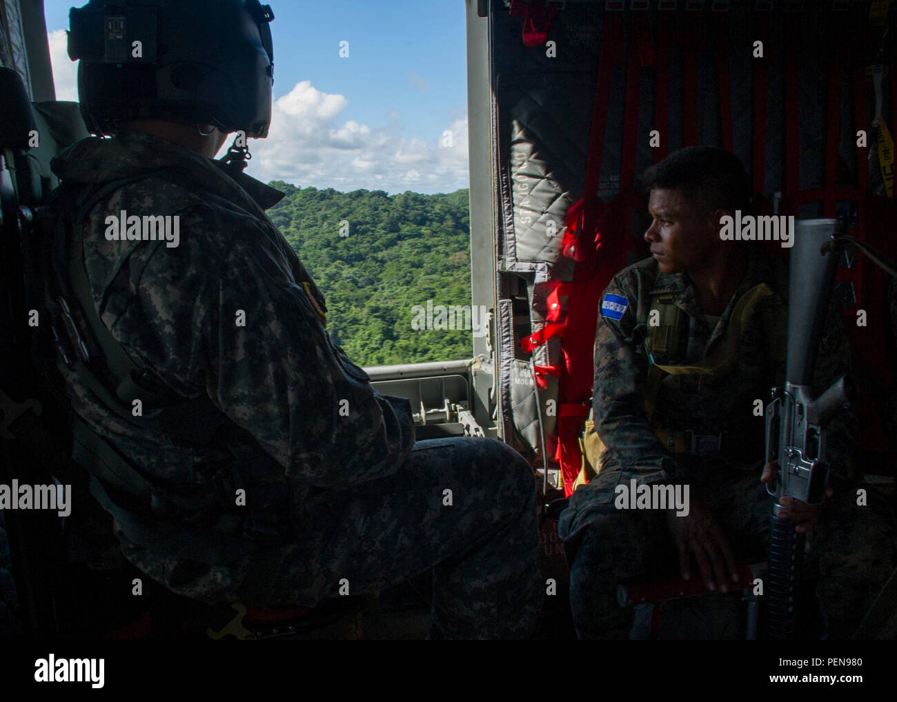 David Uplinger 1-228th Aviation Regiment flight engineer and a Honduran troop watch the trees slip by the door of a U.S. Army CH-47 Chinook Dec. 17, 2015, as they fly over the Gracias a Dios Department (state) of Honduras. The airlift for the troops is a result of a request for assistance to help disrupt the flow of drugs in the region by the Honduran president in October 2014. (U.S. Air Force photo by Capt. Christopher Mesnard/Released) Stock Photo