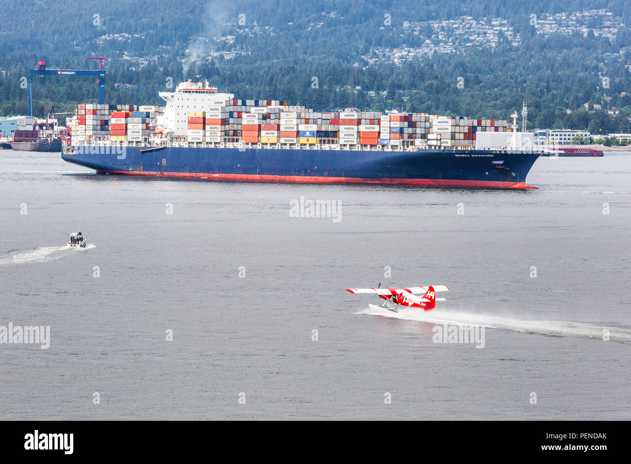 A tourist seaplane taking off in quite close proximity to the container ship Seamax Stratford in the harbour at Vancouver, British Columbia, Canada Stock Photo