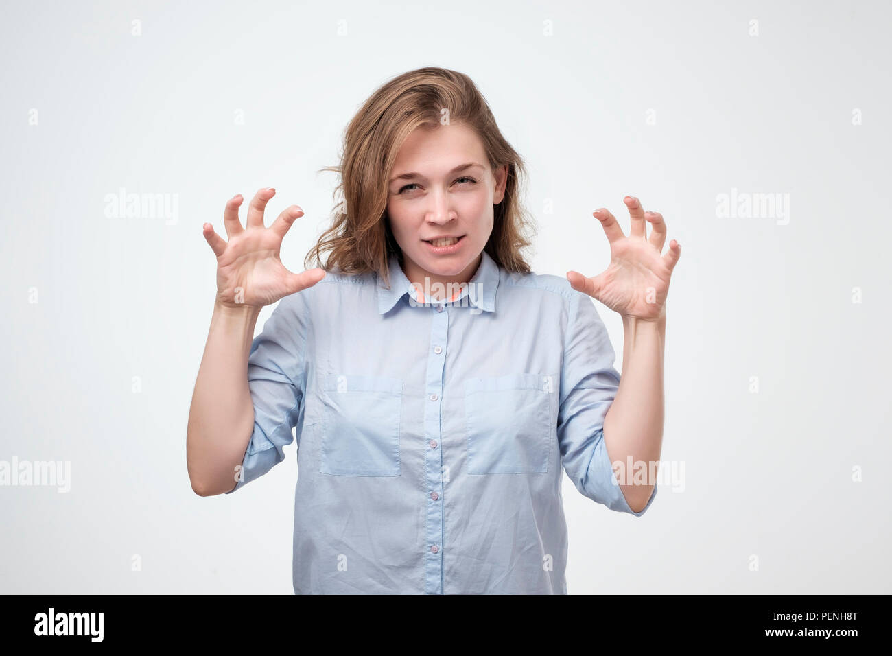 Caucasian woman showing her wild side posing in blue shirt growling at you and gesturing a claw shape with her hands, over gray background. Lose contr Stock Photo