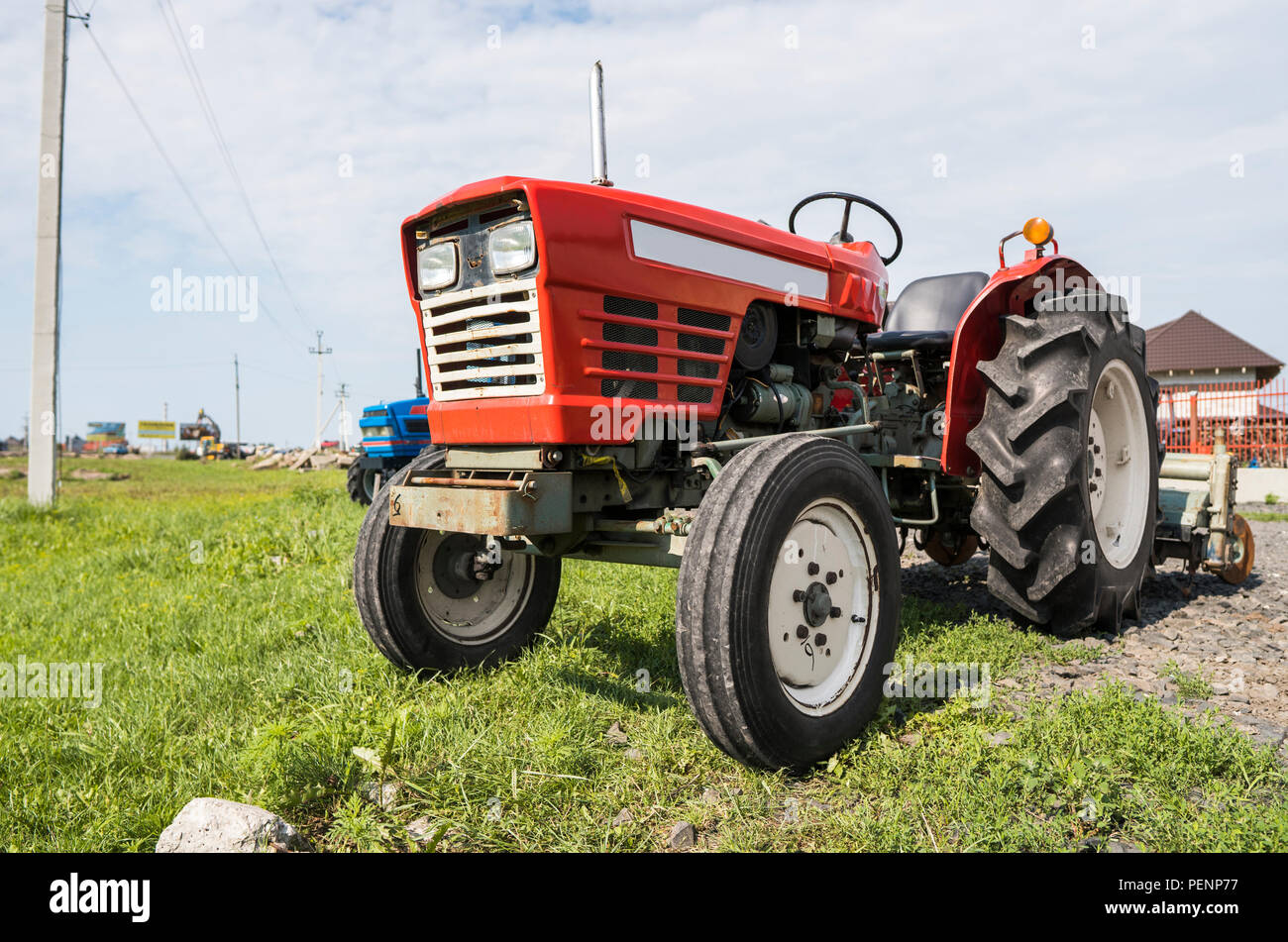 A small mini red tractor stands on a farm yard on green grass and waits for work to begin Stock Photo