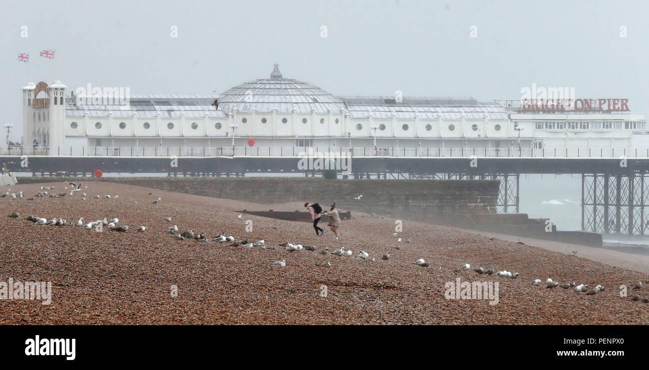 A couple walk along Brighton beach in East Sussex as outbreaks of rain sweep across the country. Stock Photo