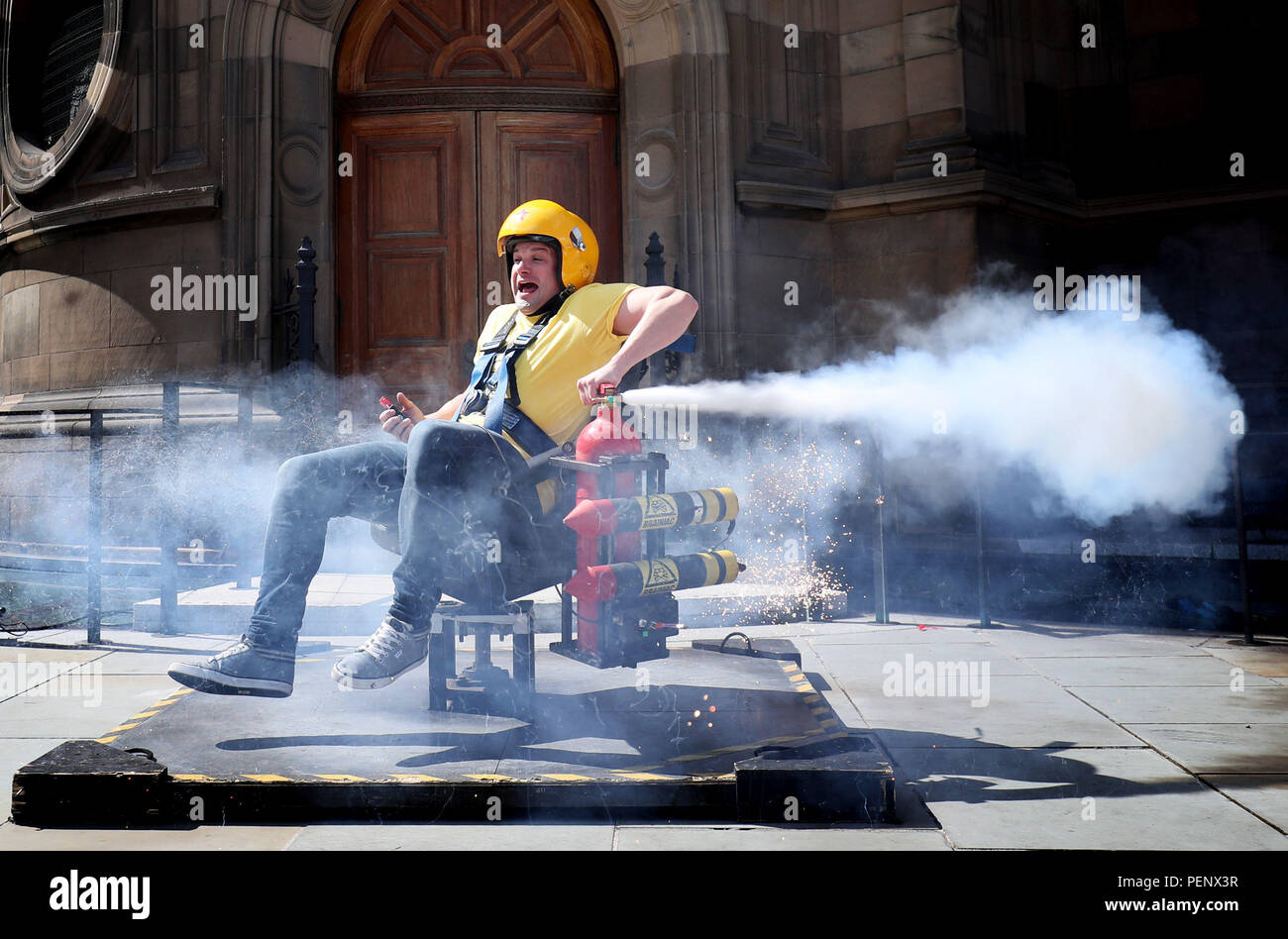 Actor Andy Joyce tests the spinning rocket chair in front of Edinburgh's McEwan Hall which forms part of one of the explosive science experiments that are demonstrated in the Edinburgh Fringe show 'Brainiac Live!'. Stock Photo