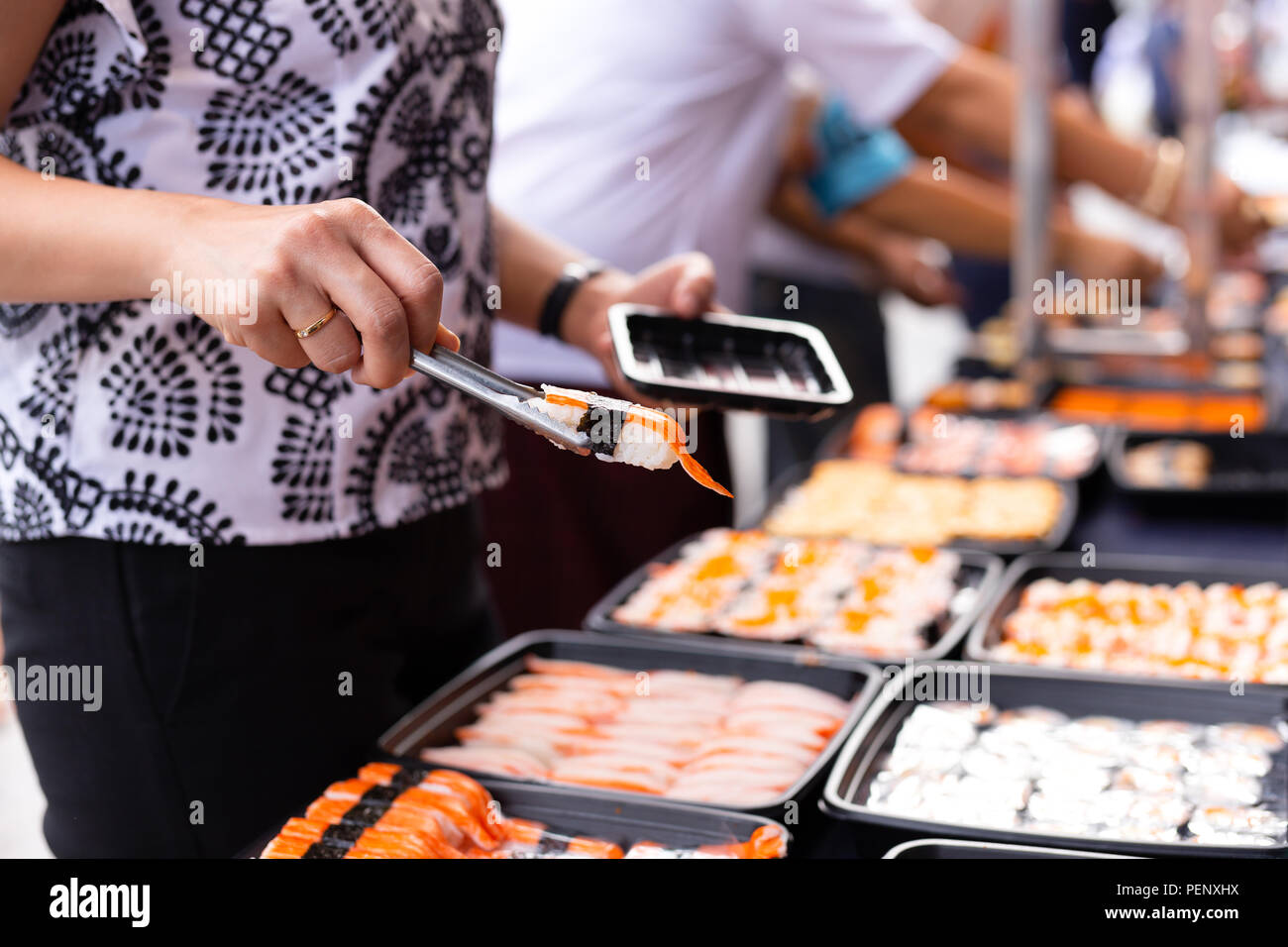 Hand picking sushi roll from food stall at event street market in Thailand. Stock Photo