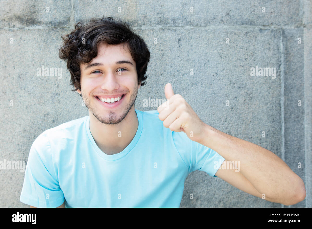 Caucasian young adult man with blue eyes showing thumb up outdoors with copy space Stock Photo
