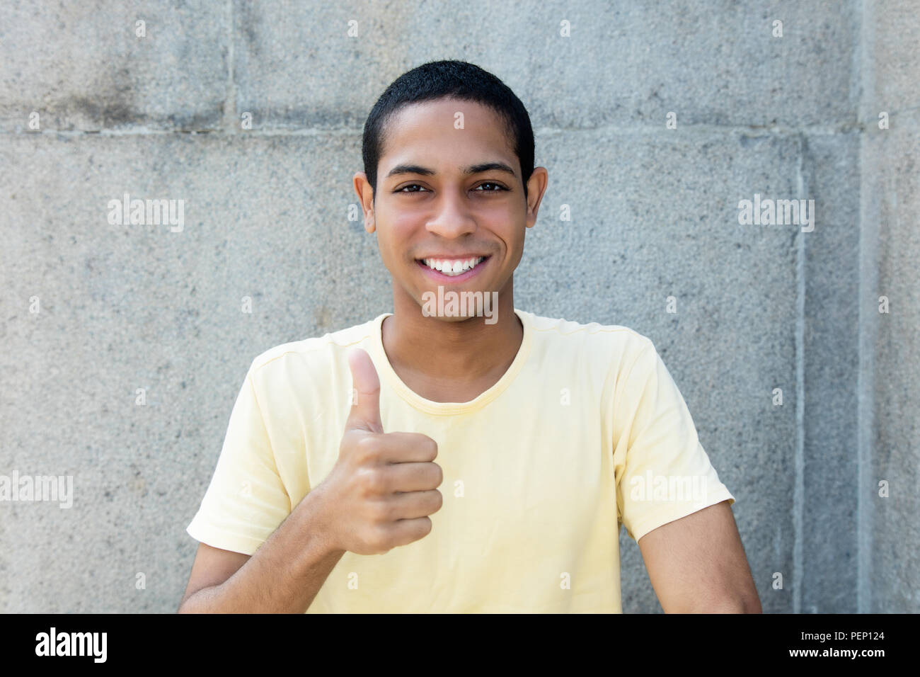 Laughing egyptian young adult man showing thumb up outdoors with copy space Stock Photo