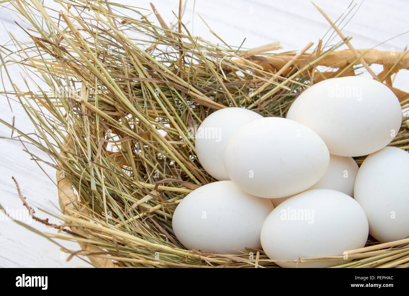 chicken eggs in basket with hay on a white wooden background. eggs on ...