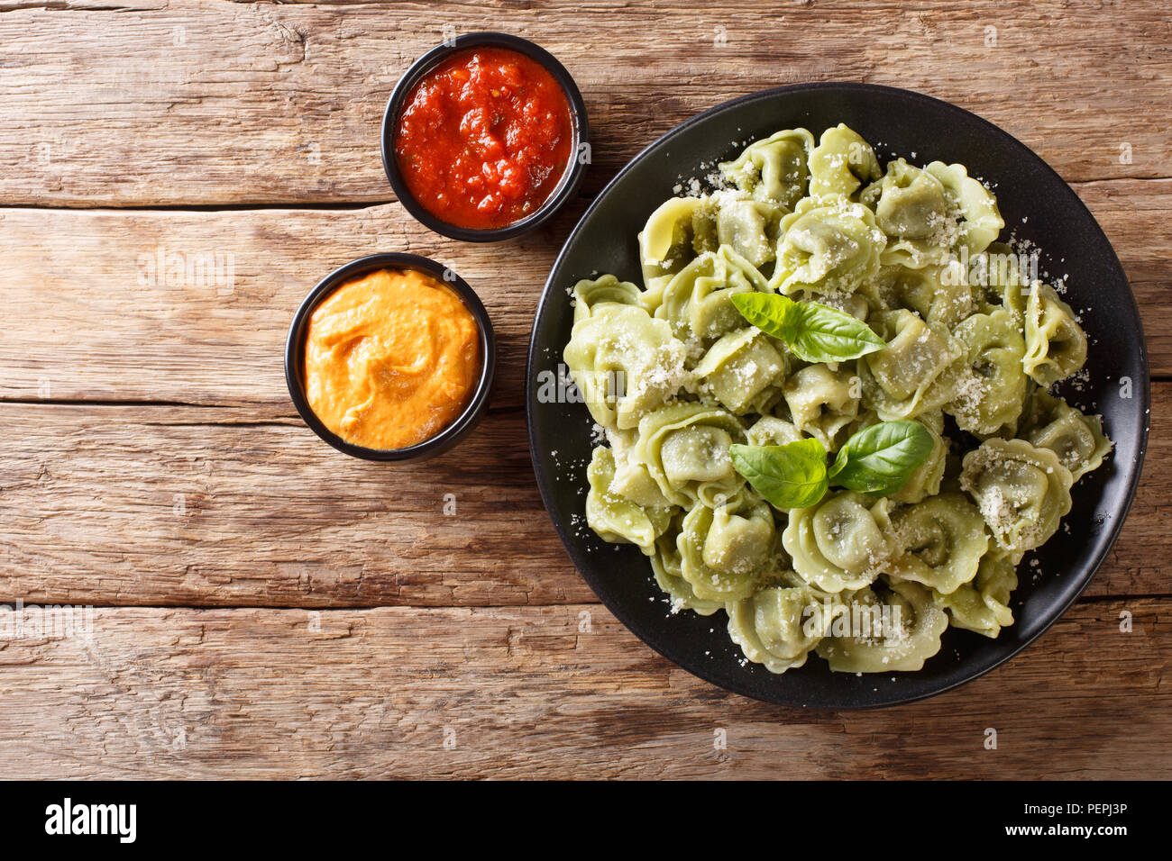 Boiled spinach green cappelletti, ravioli, tortellini stuffed with meat with parmesan cheese and basil served with sauces close-up on the table. horiz Stock Photo