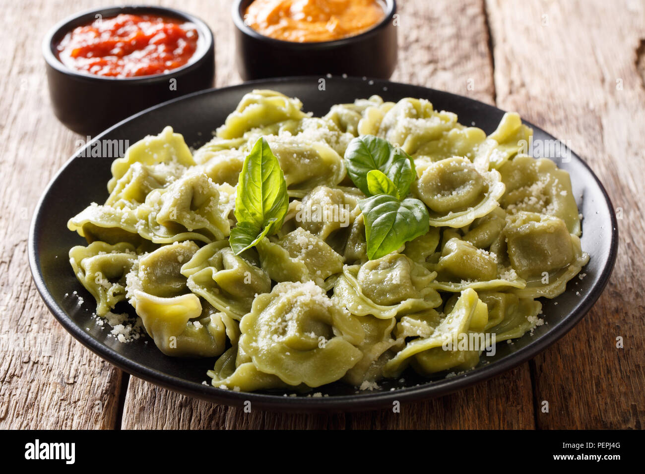 Delicious spinach green cappelletti, ravioli, tortellini with parmesan cheese, basil, sauces close-up on the table. horizontal Stock Photo