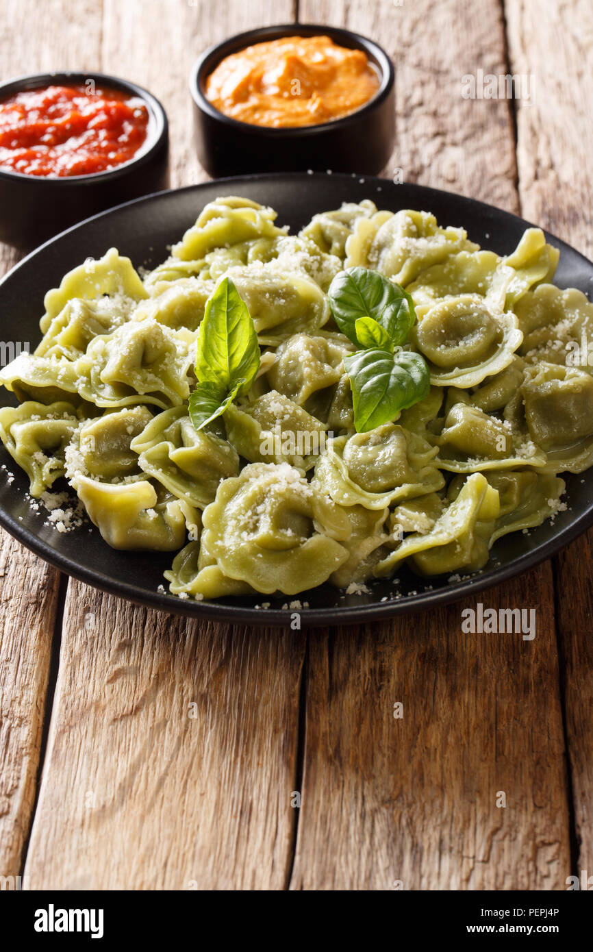 Boiled spinach green cappelletti, ravioli, tortellini stuffed with meat with parmesan cheese and basil served with sauces close-up on the table. verti Stock Photo