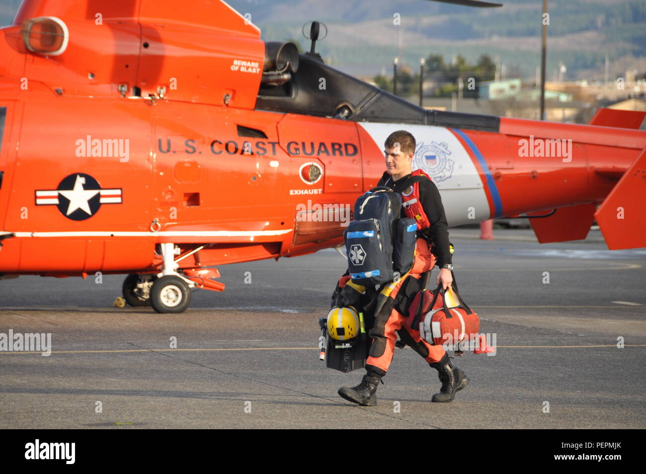 A Coast Guard rescue swimmer carries gear to an MH-65 Dolphin helicopter before launching for a search-and-rescue case near Coos Bay, Ore., Jan. 26, 2016. Two Dolphin helicopter crews and two 47-foot Motor Lifeboat crews rescued three men from the water in 12-to-14-foot seas after the 49-foot fishing vessel Sara Jo capsized on the Coos Bay bar. (U.S. Coast Guard photo by Lt. Wes Jones) Stock Photo
