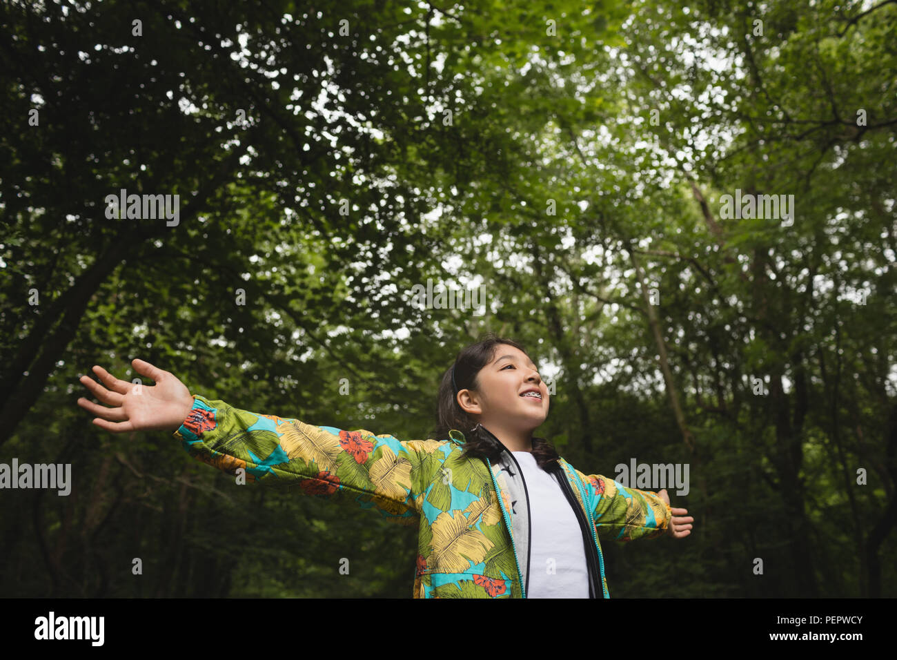 Girl with arms outstretched standing in forest Stock Photo