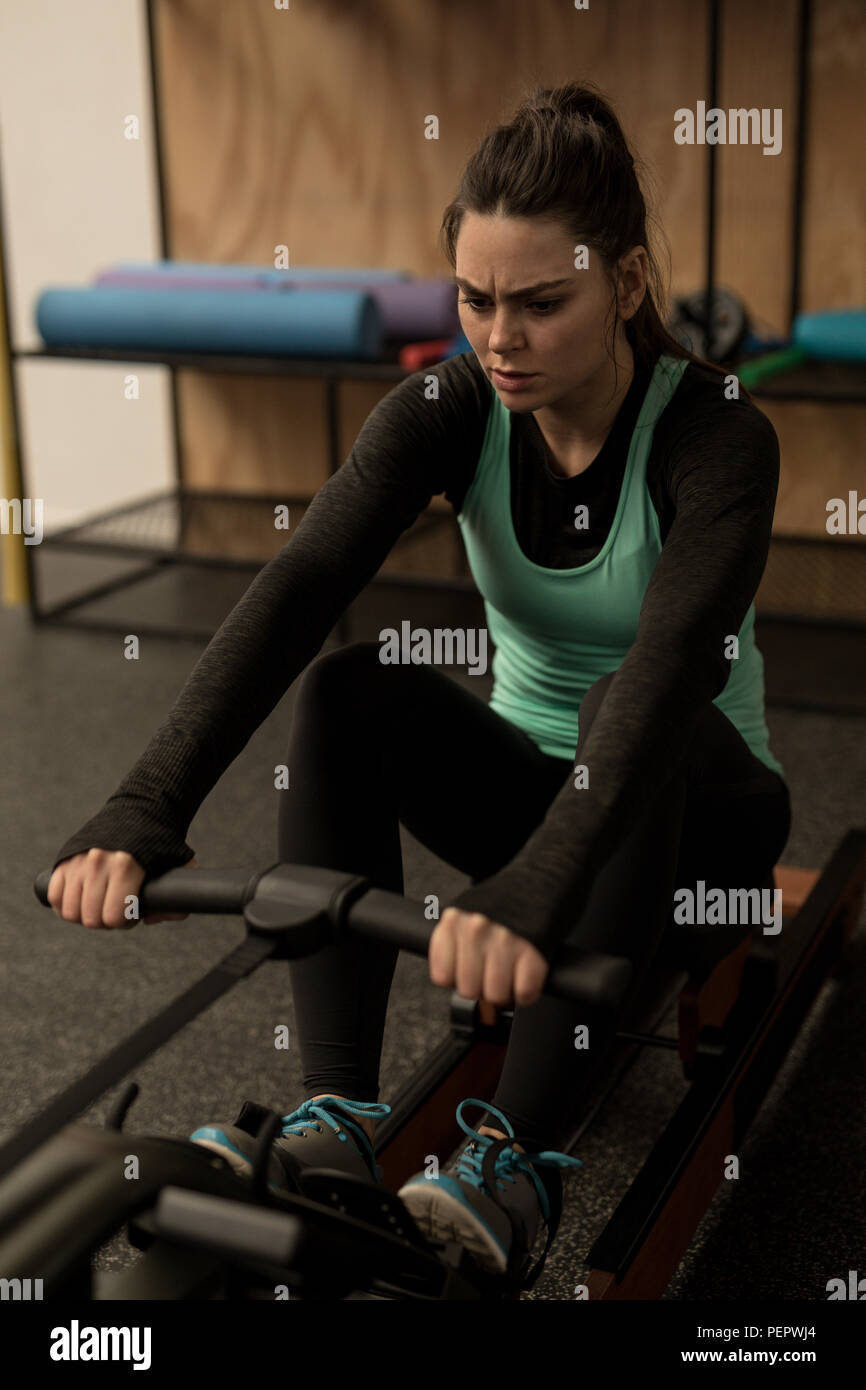Woman exercising on rowing machine in fitness studio Stock Photo