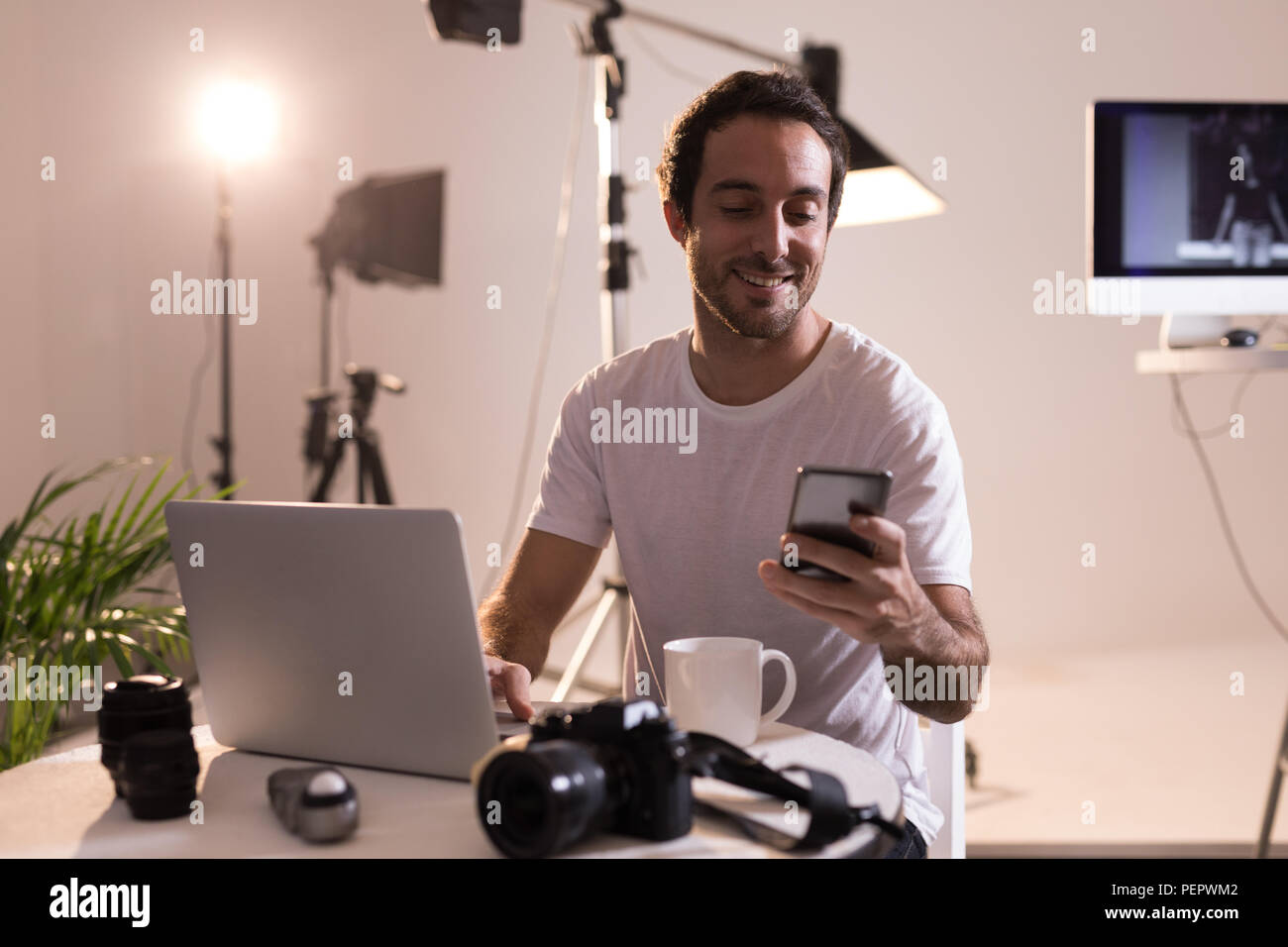 Male photographer using mobile phone while working on laptop Stock Photo